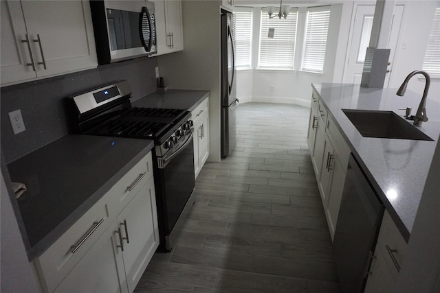 kitchen with dark wood finished floors, white cabinetry, stainless steel appliances, a sink, and baseboards