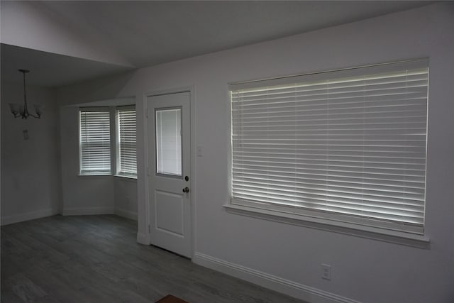 entryway with an inviting chandelier, wood finished floors, lofted ceiling, and baseboards