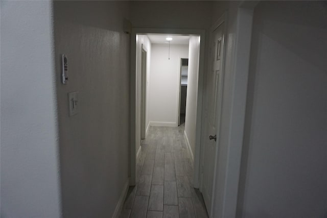 corridor with baseboards, wood finished floors, and attic access