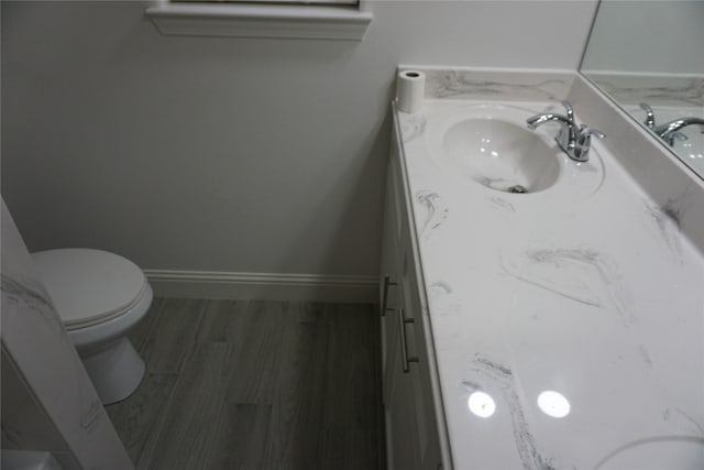 bathroom with baseboards, wood finished floors, toilet, and vanity