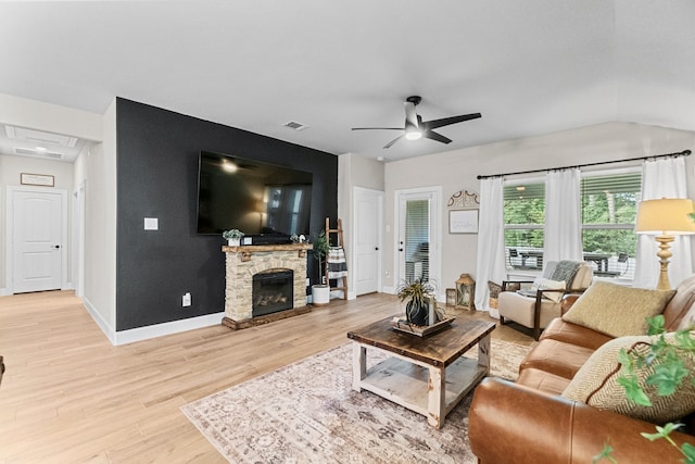 living room featuring ceiling fan, light wood-type flooring, lofted ceiling, and a stone fireplace