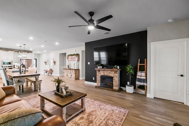 living room with ceiling fan, light hardwood / wood-style floors, and a stone fireplace