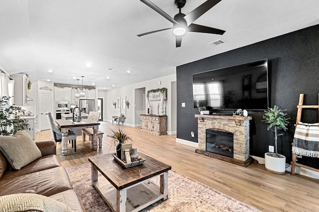 living room with light hardwood / wood-style flooring, ceiling fan with notable chandelier, and a stone fireplace