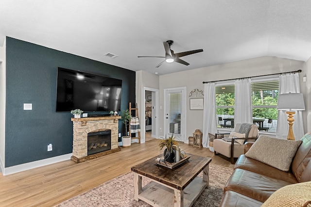 living room with ceiling fan, vaulted ceiling, light hardwood / wood-style flooring, and a stone fireplace