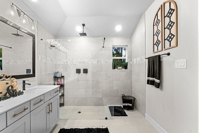 bathroom with a tile shower, vanity, tile patterned floors, tile walls, and lofted ceiling