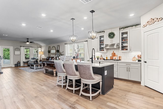 kitchen with ceiling fan with notable chandelier, light hardwood / wood-style floors, plenty of natural light, and an island with sink