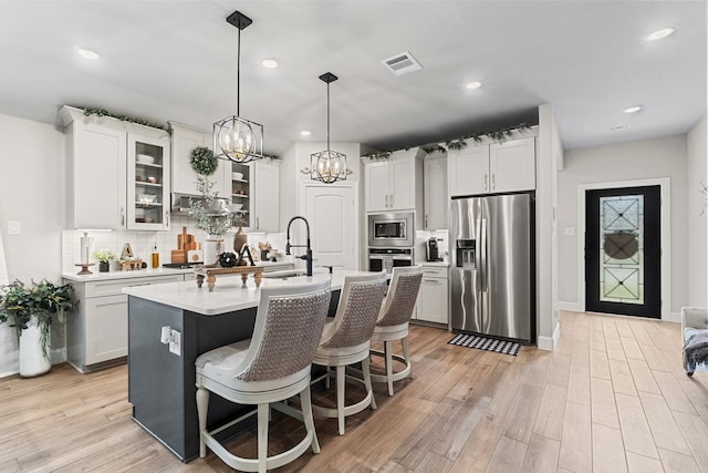 kitchen featuring a kitchen bar, light hardwood / wood-style floors, a kitchen island with sink, tasteful backsplash, and stainless steel appliances