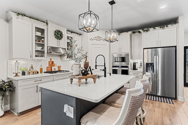 kitchen with stainless steel appliances, a center island with sink, decorative backsplash, and light hardwood / wood-style floors