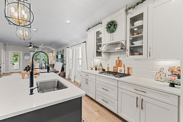 kitchen featuring ceiling fan with notable chandelier, vaulted ceiling, stainless steel gas stovetop, white cabinetry, and hanging light fixtures