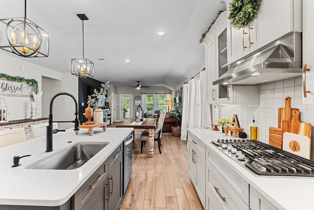 kitchen featuring backsplash, light hardwood / wood-style floors, pendant lighting, ceiling fan with notable chandelier, and vaulted ceiling