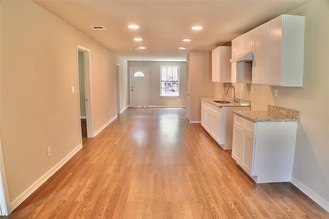 kitchen featuring light hardwood / wood-style flooring, sink, light stone countertops, and white cabinetry