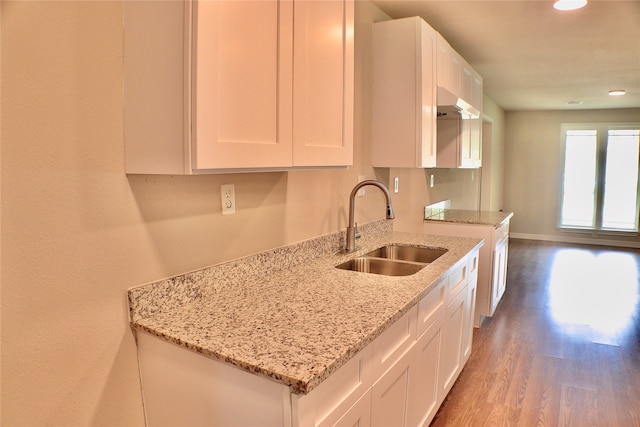 kitchen featuring light stone countertops, wood-type flooring, sink, and white cabinets