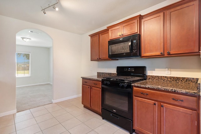 kitchen featuring dark stone countertops, arched walkways, brown cabinetry, and black appliances