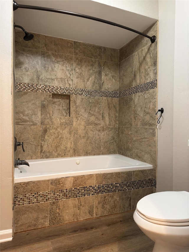 bathroom featuring hardwood / wood-style flooring, tiled shower / bath, and toilet