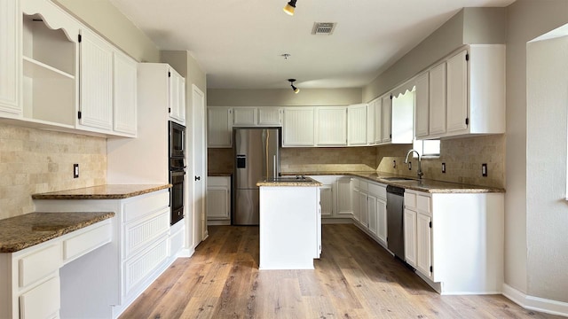 kitchen with stone counters, appliances with stainless steel finishes, light hardwood / wood-style flooring, and a kitchen island