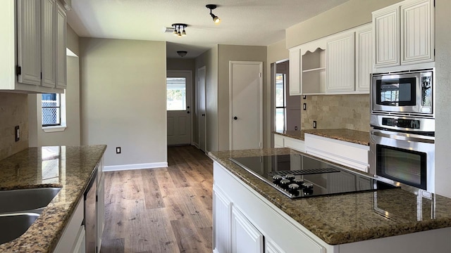 kitchen featuring dark stone countertops, light hardwood / wood-style floors, tasteful backsplash, white cabinetry, and stainless steel appliances