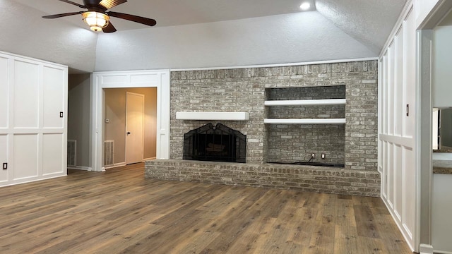 unfurnished living room featuring vaulted ceiling, dark hardwood / wood-style floors, a textured ceiling, ceiling fan, and a brick fireplace