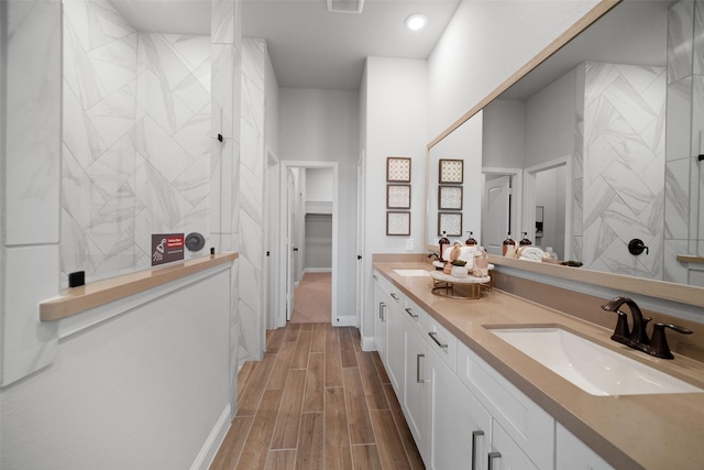 bathroom featuring visible vents, wood finish floors, tiled shower, double vanity, and a sink