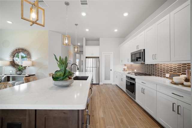 kitchen featuring appliances with stainless steel finishes, decorative backsplash, white cabinetry, sink, and pendant lighting