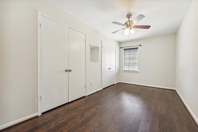 unfurnished bedroom featuring dark wood-type flooring, ceiling fan, and multiple closets