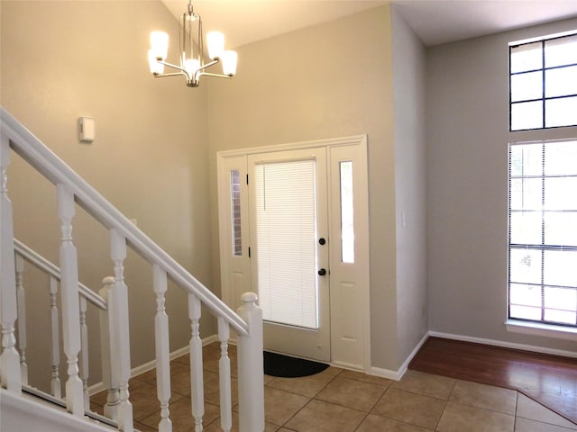 entryway featuring a notable chandelier, a high ceiling, light tile patterned floors, baseboards, and stairs