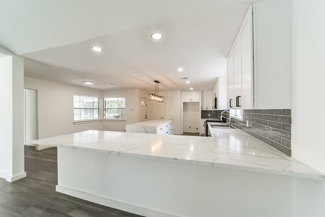 kitchen with kitchen peninsula, light stone counters, decorative light fixtures, and dark hardwood / wood-style flooring