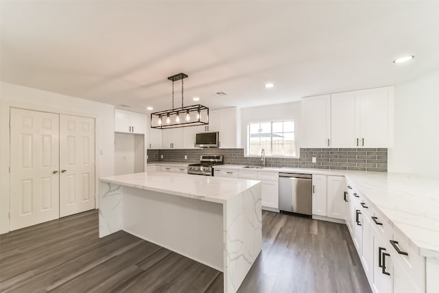 kitchen featuring dark hardwood / wood-style flooring, hanging light fixtures, appliances with stainless steel finishes, light stone countertops, and sink