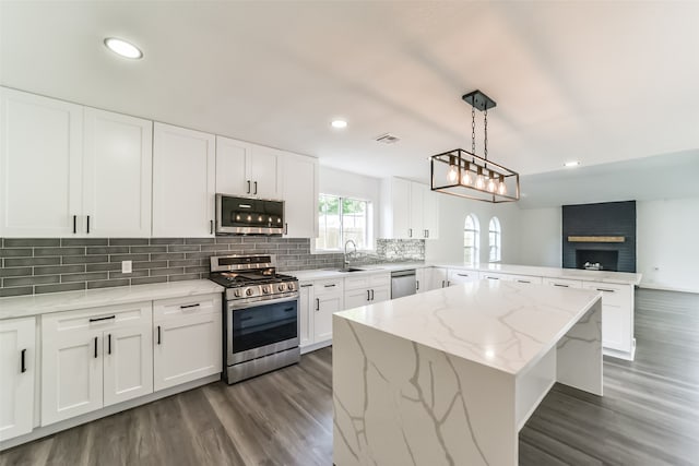 kitchen featuring appliances with stainless steel finishes, decorative light fixtures, dark hardwood / wood-style floors, light stone counters, and a brick fireplace