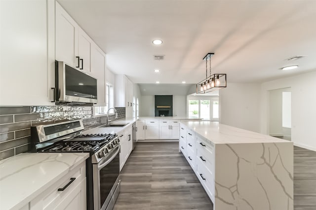 kitchen featuring sink, appliances with stainless steel finishes, light stone counters, dark hardwood / wood-style floors, and hanging light fixtures