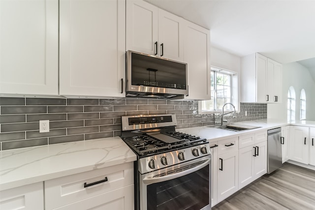 kitchen featuring appliances with stainless steel finishes, white cabinetry, sink, light stone counters, and light wood-type flooring