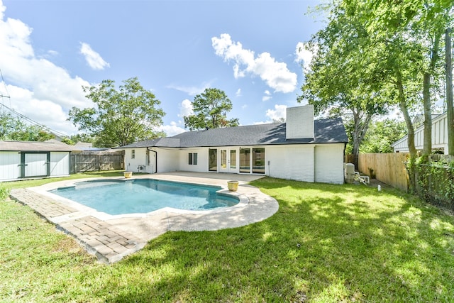 view of swimming pool featuring a patio, a lawn, and an outbuilding