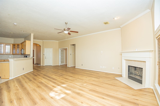 unfurnished living room with ceiling fan, light hardwood / wood-style flooring, a tile fireplace, and ornamental molding