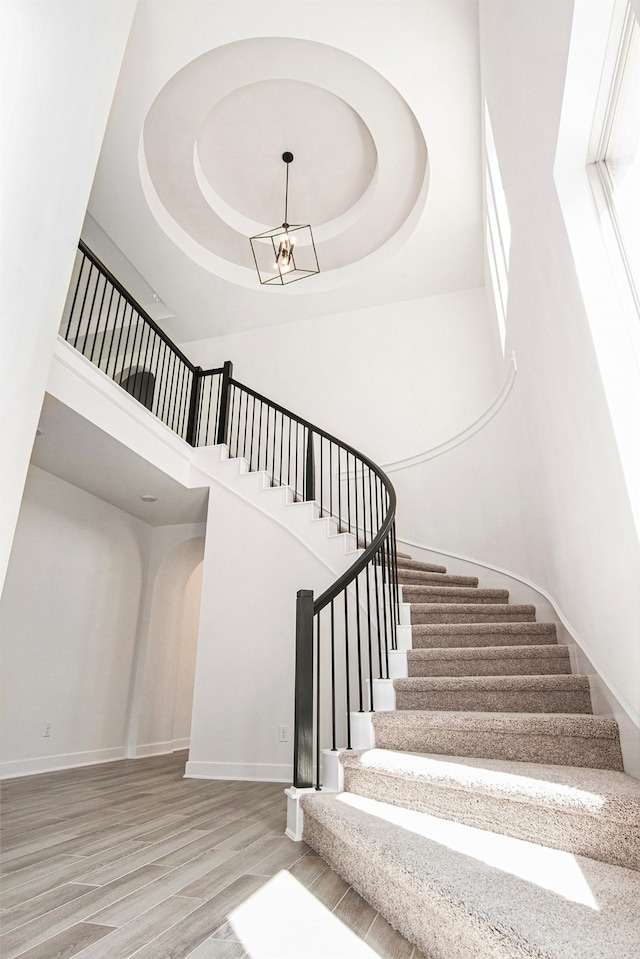 stairs featuring wood-type flooring, a towering ceiling, an inviting chandelier, and a raised ceiling