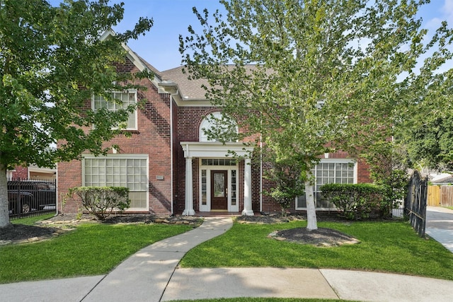 view of front facade with brick siding, fence, and a front lawn