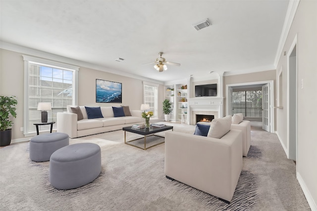 living room with ceiling fan, ornamental molding, light carpet, and built in shelves