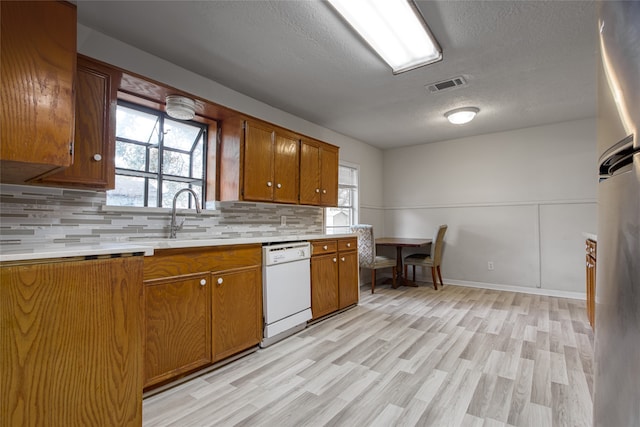 kitchen featuring backsplash, light hardwood / wood-style floors, white dishwasher, sink, and a textured ceiling