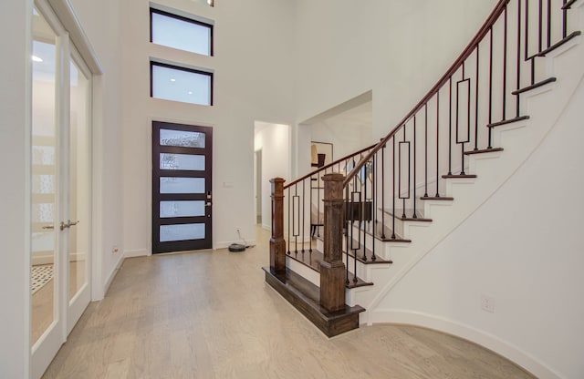 entrance foyer with a towering ceiling, french doors, and light hardwood / wood-style floors