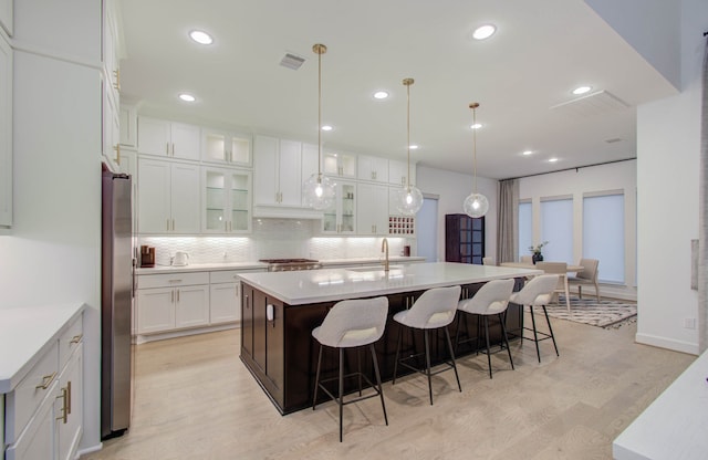 kitchen featuring decorative light fixtures, decorative backsplash, an island with sink, light hardwood / wood-style floors, and white cabinets