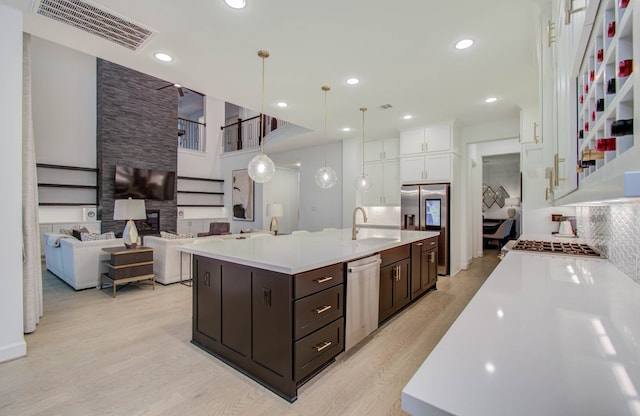 kitchen featuring backsplash, an island with sink, light hardwood / wood-style floors, appliances with stainless steel finishes, and sink