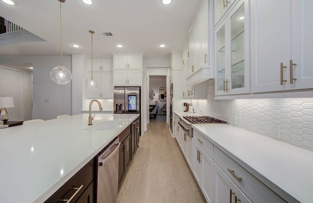 kitchen featuring decorative backsplash, light wood-type flooring, pendant lighting, white cabinetry, and stainless steel appliances