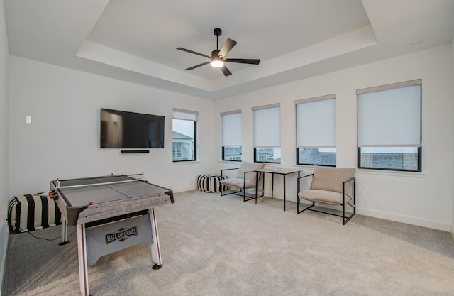 recreation room with ceiling fan, a raised ceiling, and light carpet