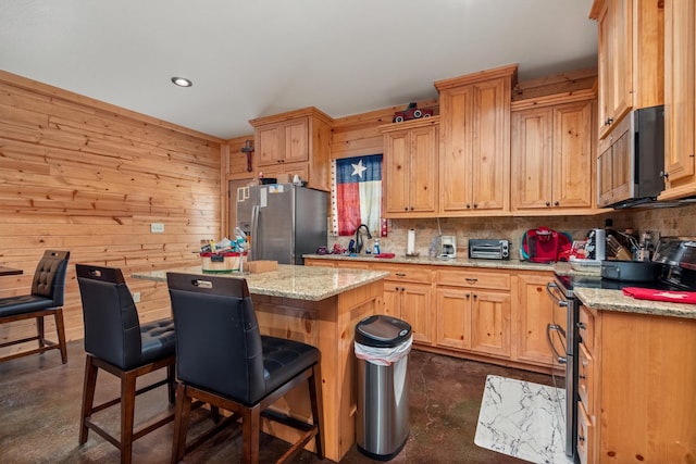 kitchen with backsplash, light stone counters, stainless steel appliances, wooden walls, and a kitchen island