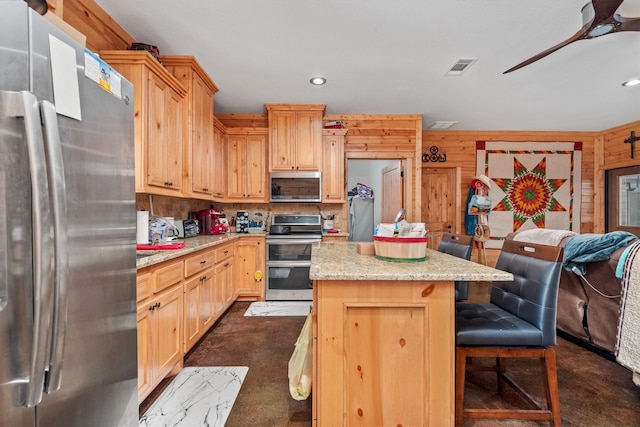 kitchen featuring wood walls, light brown cabinetry, a kitchen island, and appliances with stainless steel finishes