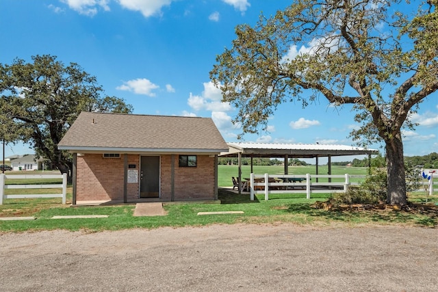 view of front of property with a front yard, an outbuilding, brick siding, fence, and a shingled roof