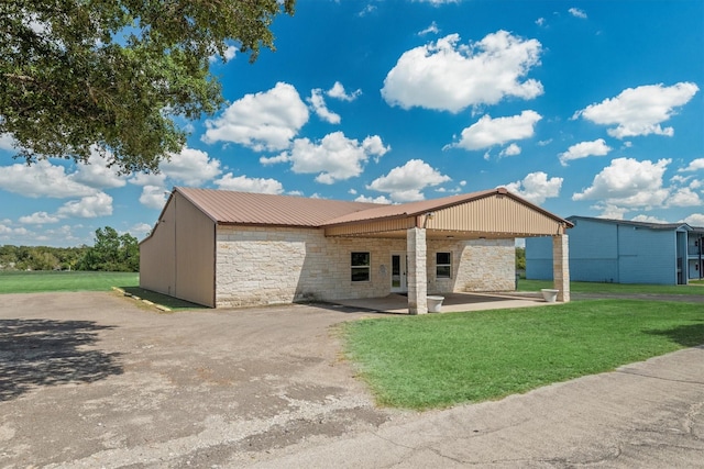 back of house featuring a yard, metal roof, a patio area, and stone siding