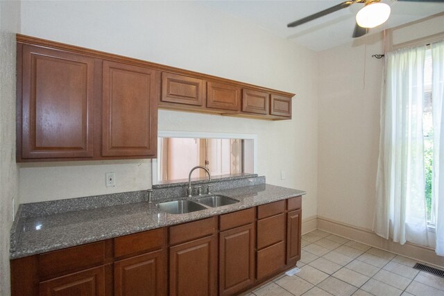 kitchen featuring sink, dark stone countertops, light tile patterned flooring, and ceiling fan