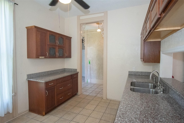 kitchen with dark countertops, glass insert cabinets, a sink, and light tile patterned flooring