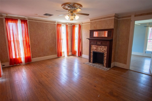 unfurnished living room with ceiling fan, wood finished floors, visible vents, a high end fireplace, and ornamental molding