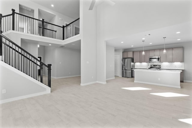 unfurnished living room featuring a high ceiling, ceiling fan, sink, and light hardwood / wood-style floors