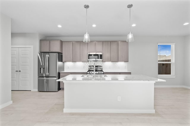 kitchen with a kitchen island with sink, hanging light fixtures, backsplash, stainless steel appliances, and light stone counters